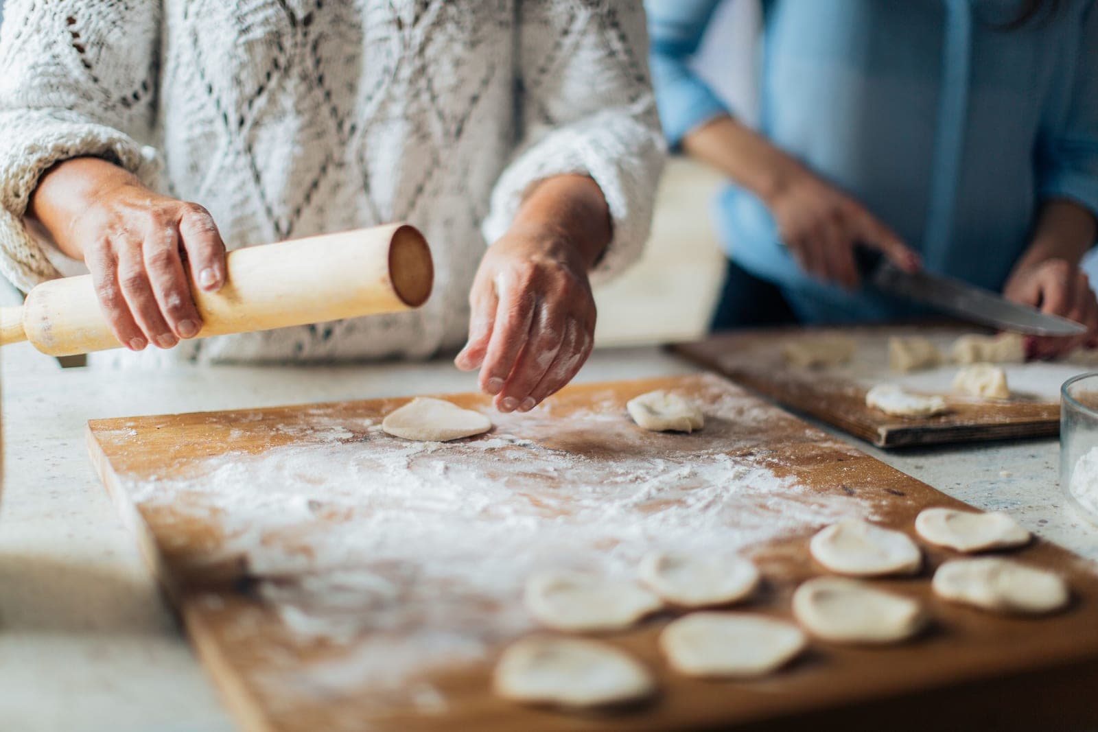 Hands rolling and shaping dough on a floured wooden board